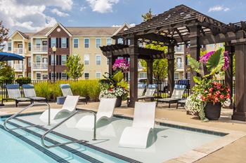 A pool with chairs and a pergola in front of a building.